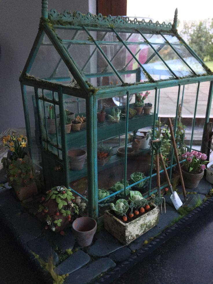 a small green house with plants and gardening tools in front of it on top of a table