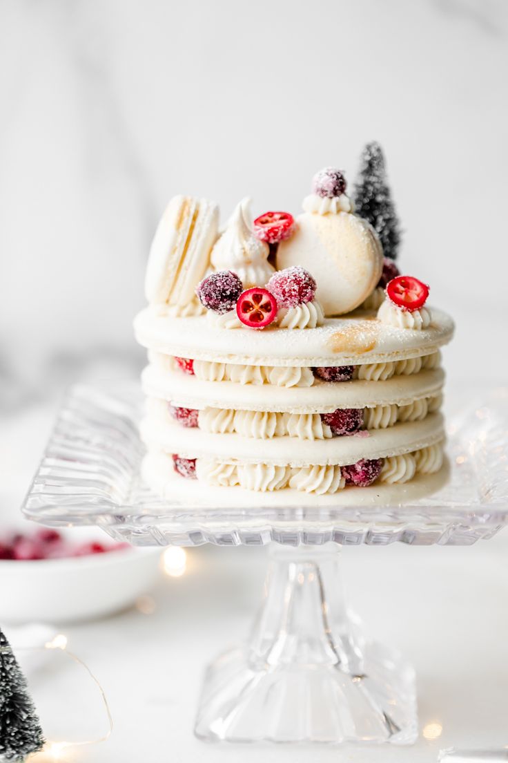 a cake with white frosting and red berries on top is sitting on a glass platter