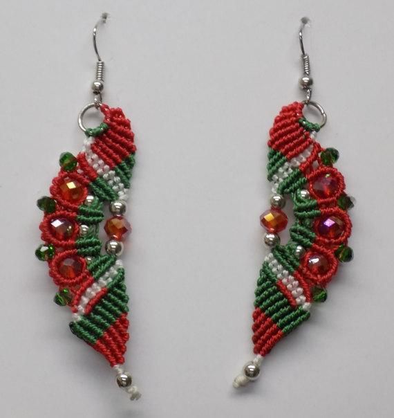 two red and green beaded earrings hanging from hooks on a white surface with beads