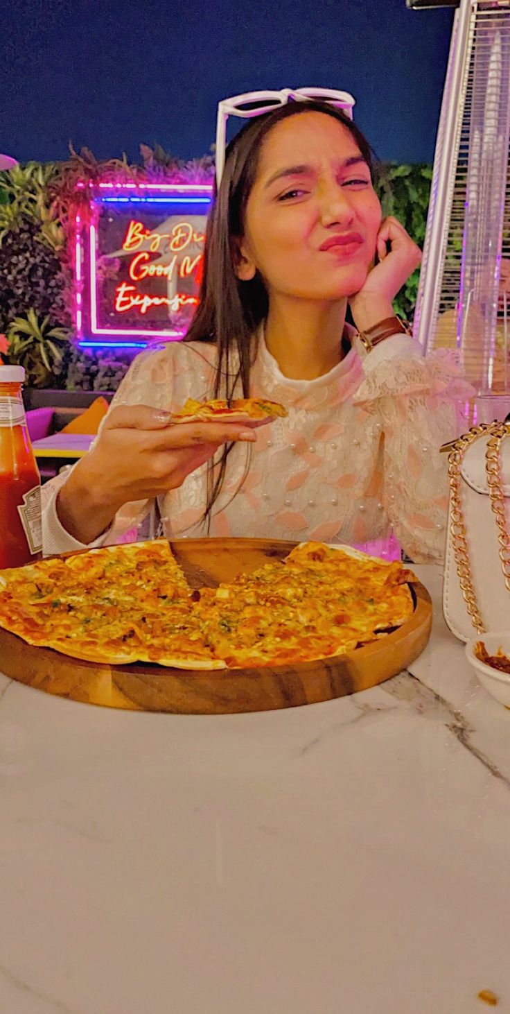 a woman sitting at a table with a pizza in front of her and talking on the phone