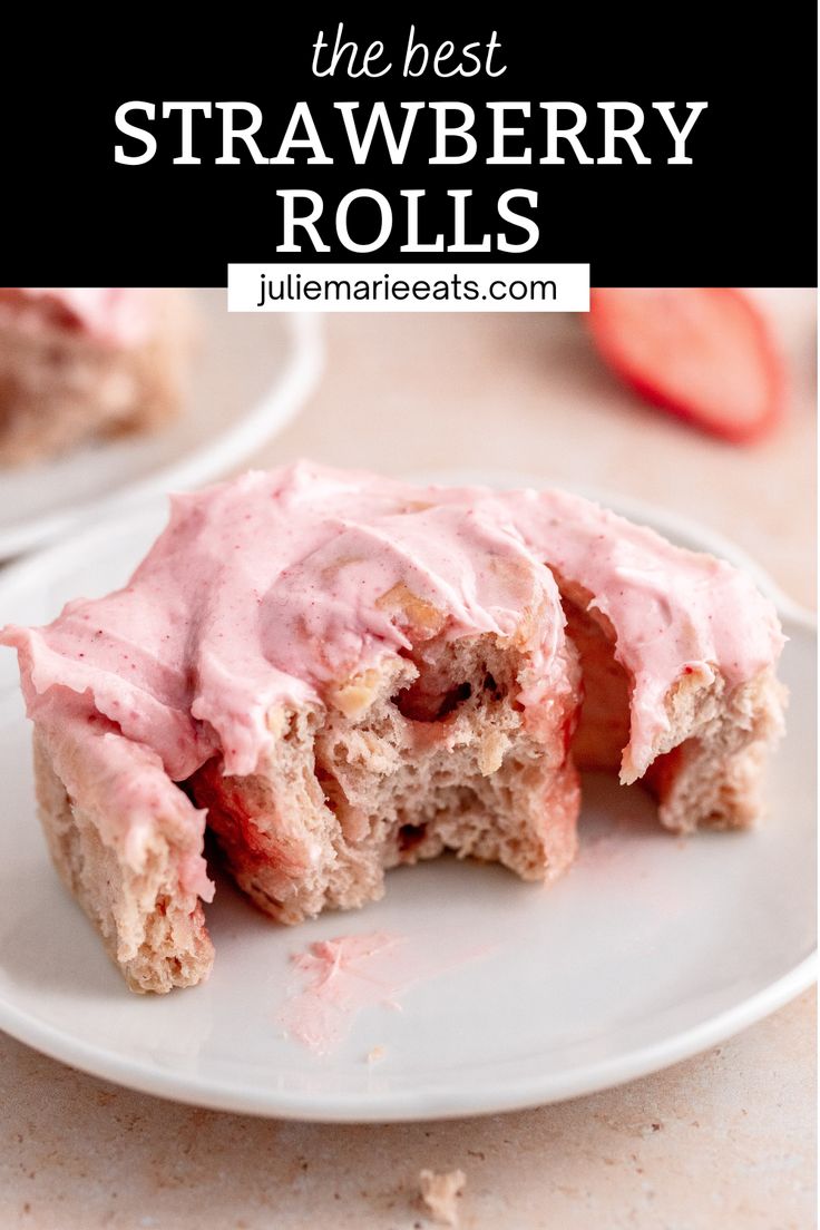 two white plates topped with pink frosted desserts next to sliced strawberries on a table