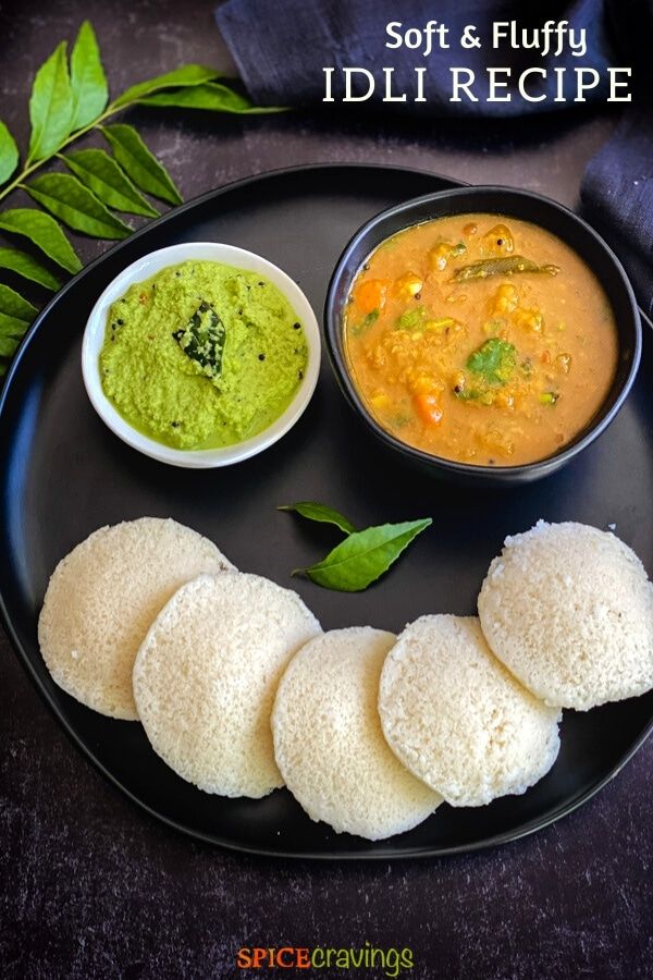 an idli is served on a black plate with green chut and sauces