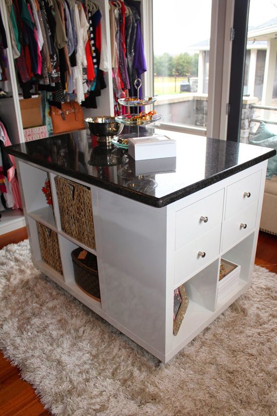 a white kitchen island with black counter top and drawers in front of a large window