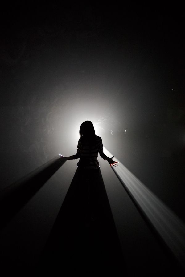 a person standing in the dark with their arms out and light shining on her head