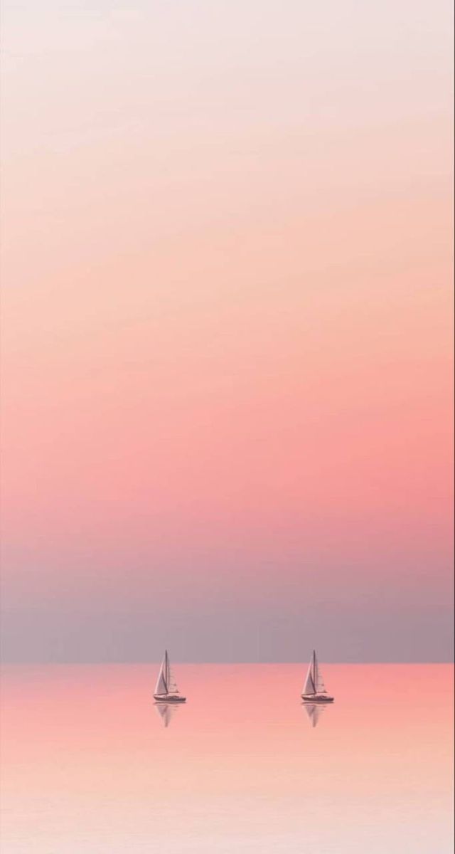 two sailboats floating in the ocean at sunset or dawn with pink and blue sky