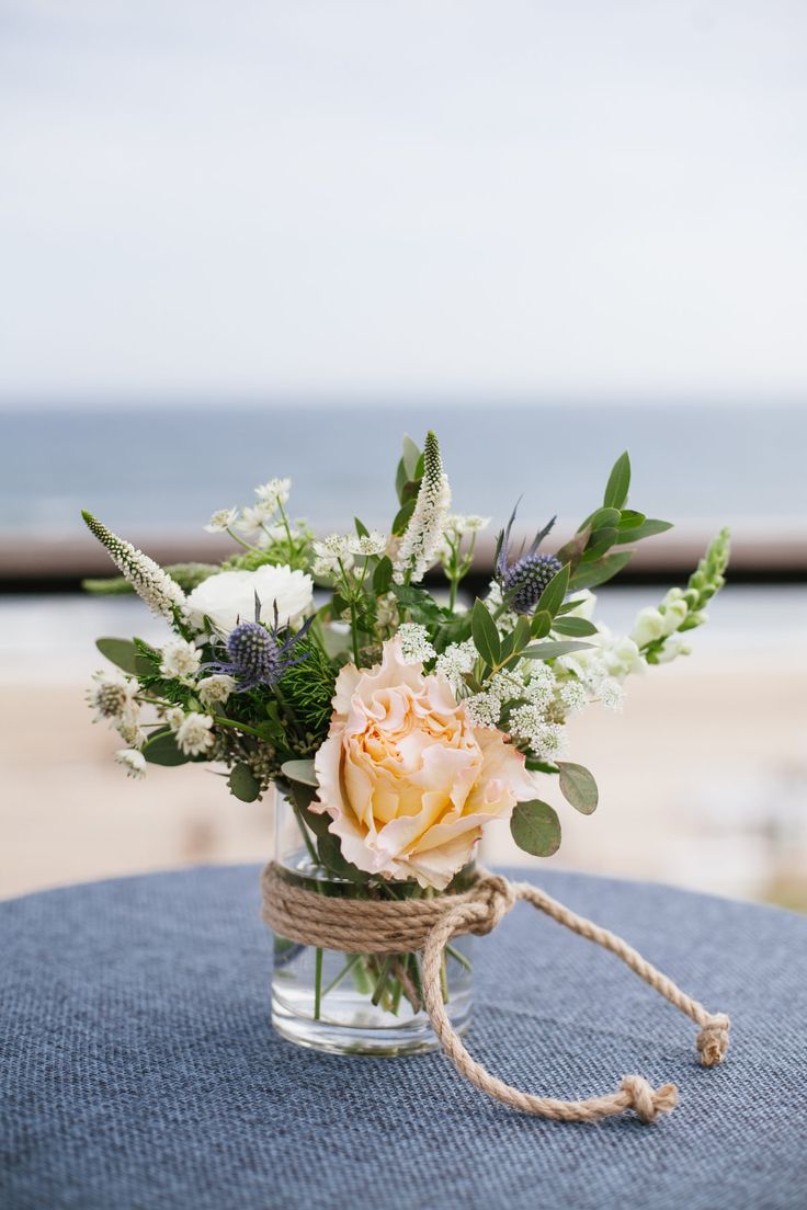 a bouquet of flowers in a glass vase on a table near the beach and water