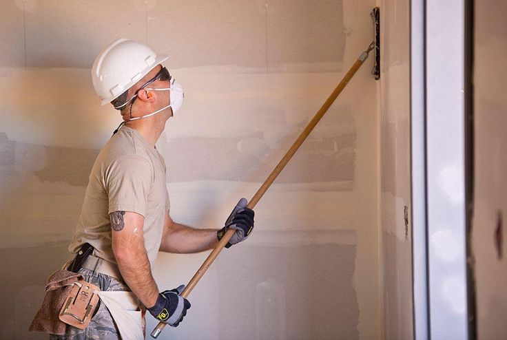 a man in a hard hat and safety glasses is painting the wall with a paint roller