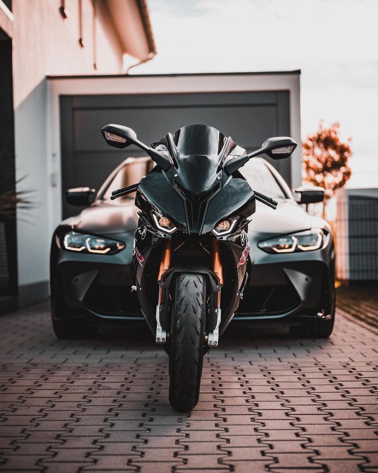 a black motorcycle parked in front of a garage next to a red and white car