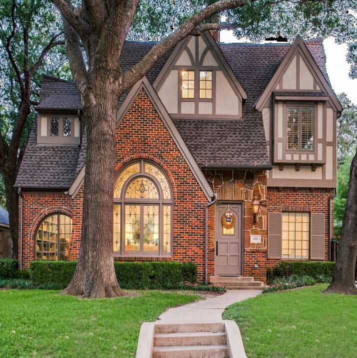 a brick house with trees and grass in the front yard at dusk, on a cloudy day