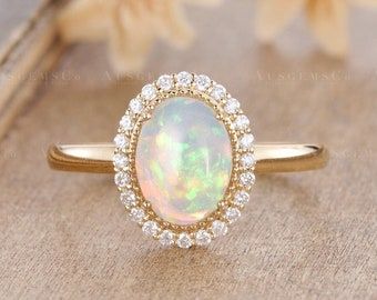 an opal and diamond ring sitting on top of a wooden table next to flowers