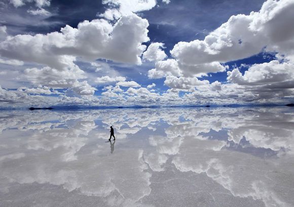 a lone person standing in the middle of a large body of water under cloudy skies