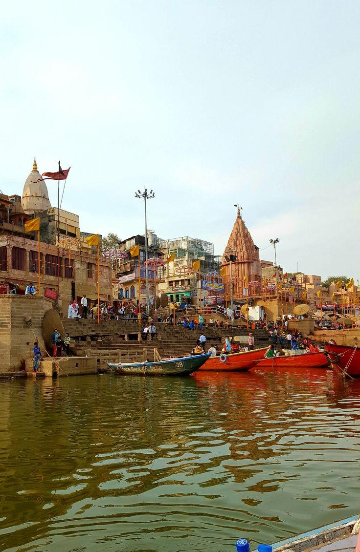 several boats are docked in the water near some buildings and people walking on the shore