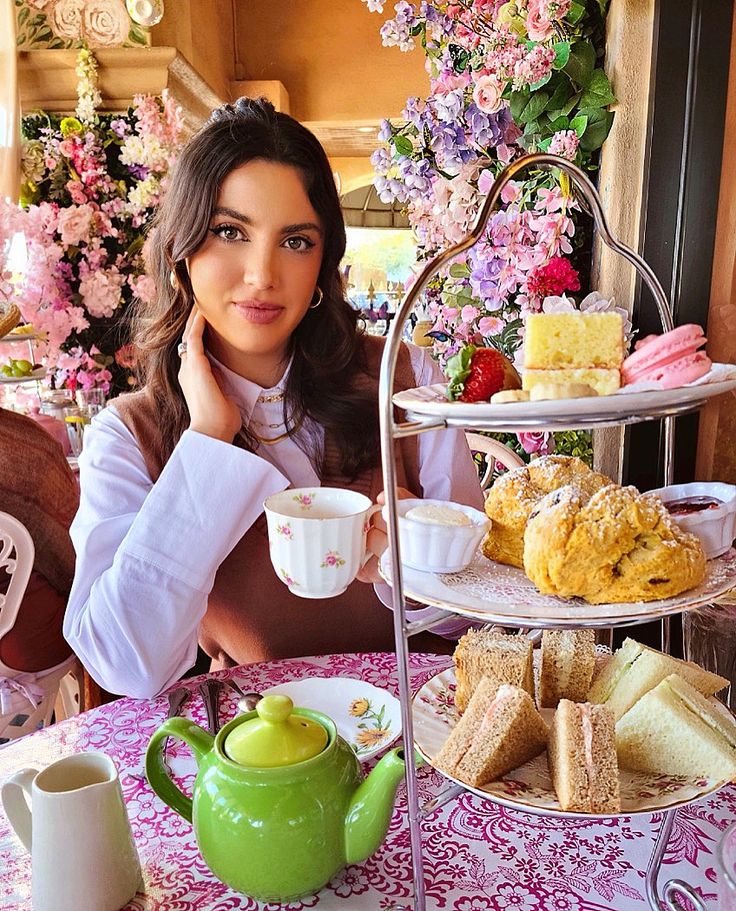 a woman sitting at a table with some food on it and a tea pot next to her