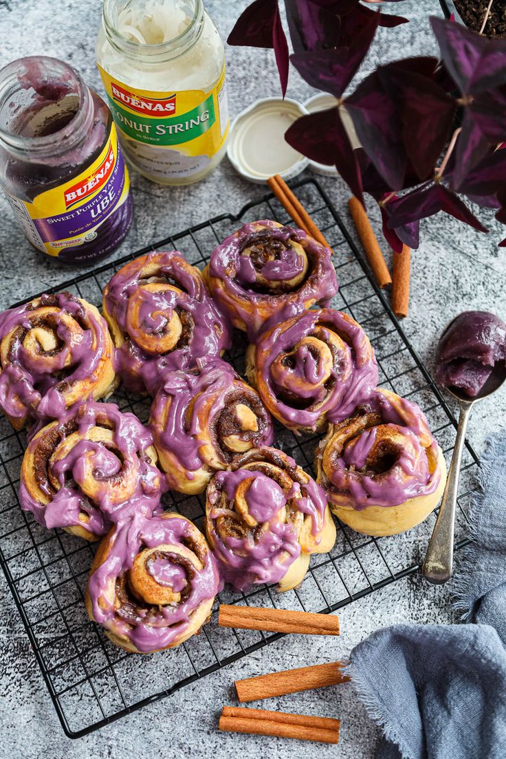 cinnamon rolls with purple icing on a cooling rack next to spices and other ingredients