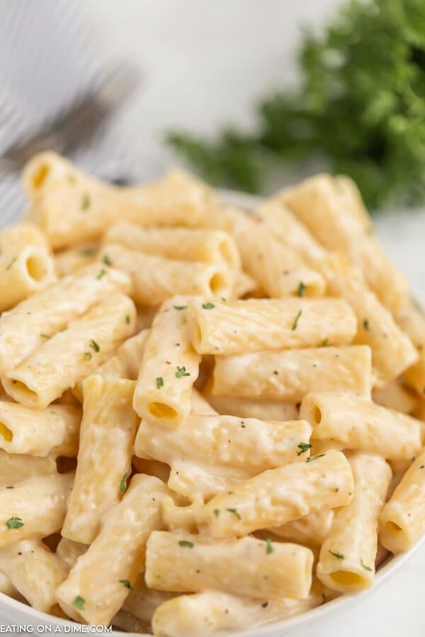 a white bowl filled with pasta and garnished with parsley on the side