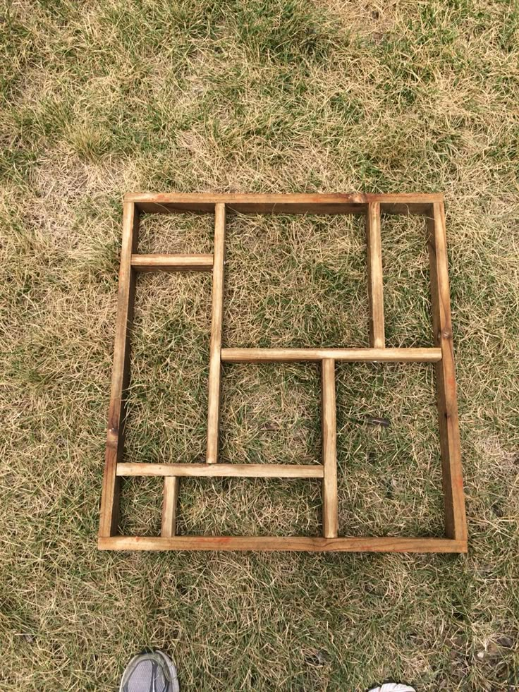 someone is standing in the grass with their feet up and looking down at a square wooden frame