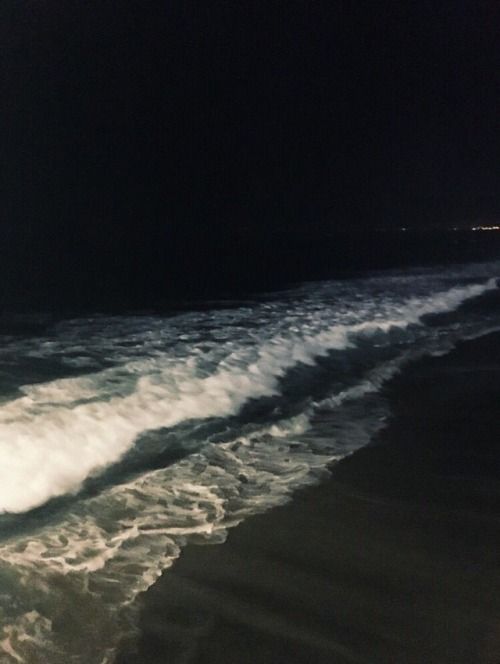 a man riding a snowboard down the side of a wave covered beach at night