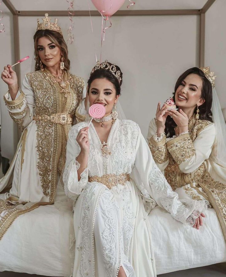 three women in white dresses sitting on a bed and one holding a lollipop