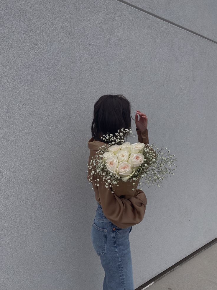 a woman standing against a wall holding a bouquet of flowers