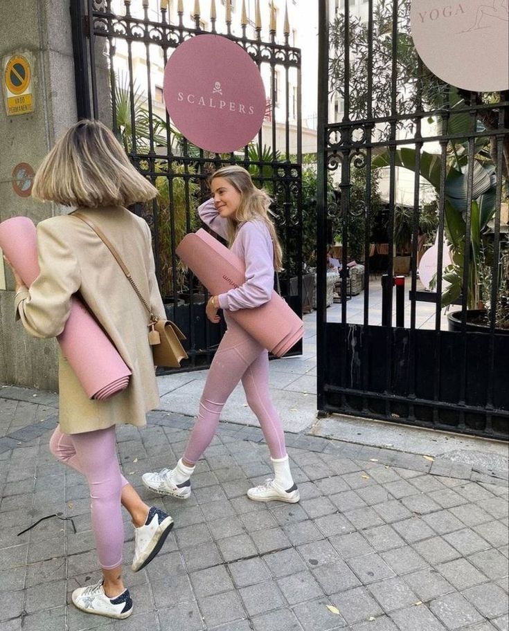 two women walking down the street in front of an iron gate with a sign on it