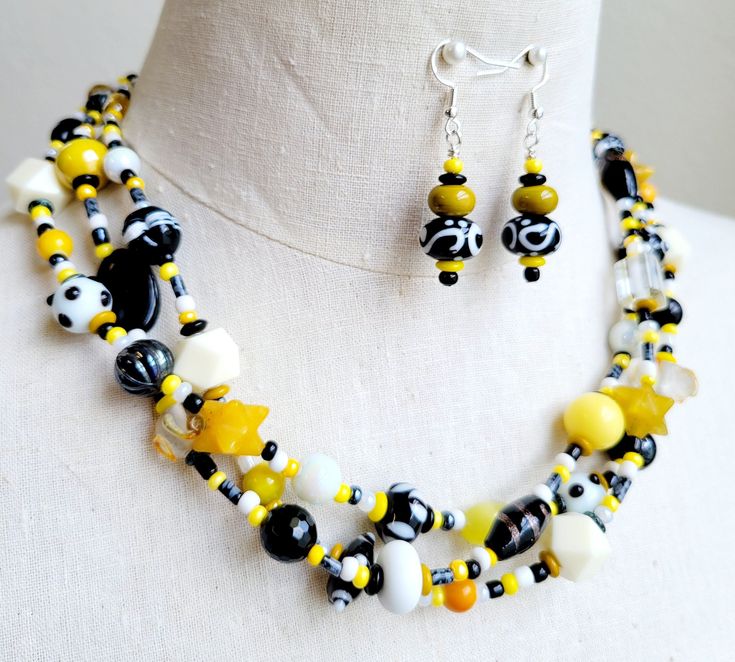 Make a real statement with this OOAK colorful necklace set. Both vintage and new glass beads, lamp work glass, jade stones, agate stones, ceramic beads, and resin beads in hues of yellow, gold, white and black are all strung on 3 wires and finished with decorative silver bead caps, a stainless-steel chain, and a large lobster clasp.  Necklace finished length is 16 inches long with an additional chain measuring 4 inches, for comfort. Matching lampwork glass beaded earrings are hung on 925 silver ear wires. Handmade Yellow Czech Glass Beaded Necklaces, Handmade Yellow Beaded Necklace With Czech Glass, Unique Yellow Jewelry With Gemstone Beads, Handmade Yellow Czech Glass Necklace, Unique Yellow Czech Glass Jewelry, Yellow Czech Glass Beaded Necklaces For Jewelry Making, Yellow Czech Glass Jewelry With Colorful Beads, Bumble Bee Necklace, Black Beaded Necklace