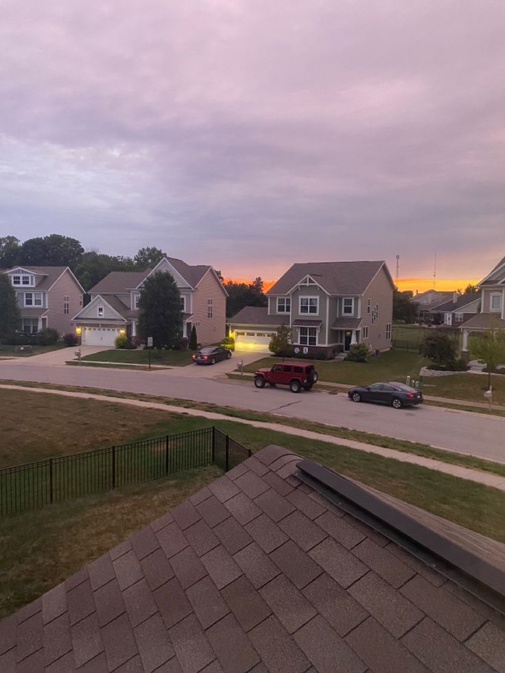 some houses and cars are parked on the side of the road at sunset or dawn