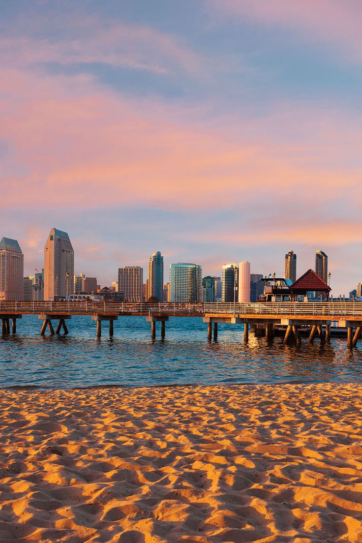 a pier with buildings in the background and sand on the beach at sunset or sunrise