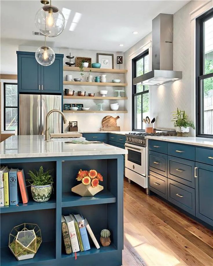 a kitchen with blue cabinets and white counter tops, an island in the middle is surrounded by bookshelves