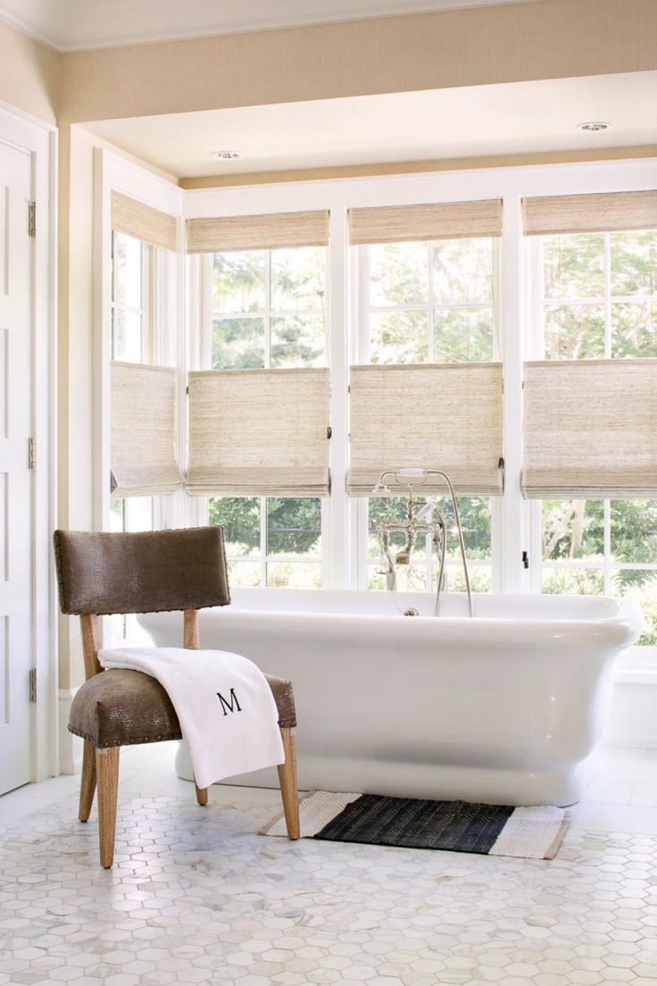 a white bath tub sitting in a bathroom next to a window with roman shades on it