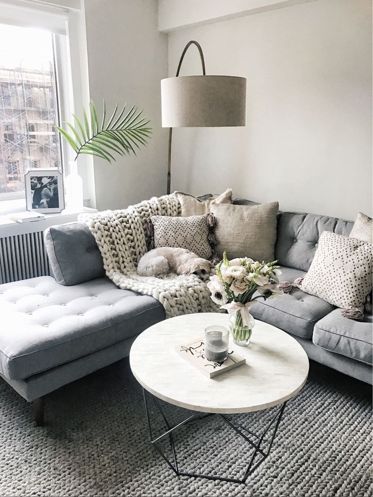 a living room with grey couches and pillows on top of the sofa, next to a large window