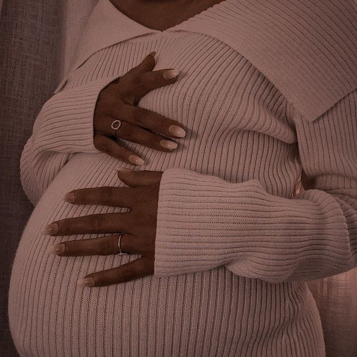 a pregnant woman with her hands wrapped around her stomach, wearing gloves and a sweater