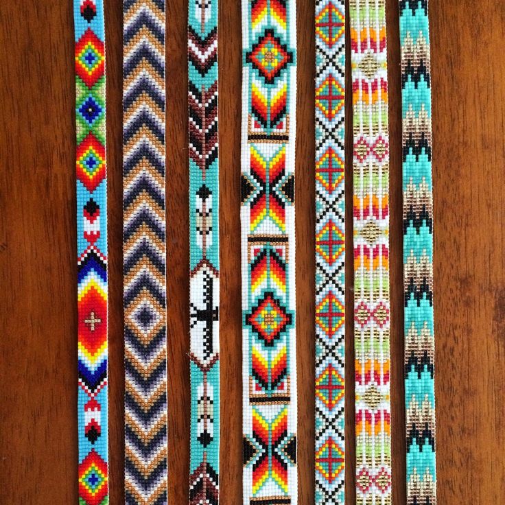 four bracelets are lined up on a wooden surface, each with different colors and designs