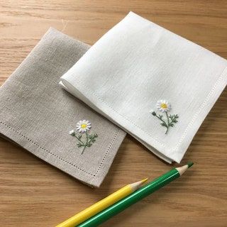 two napkins with embroidered daisies on them next to a pencil and eraser