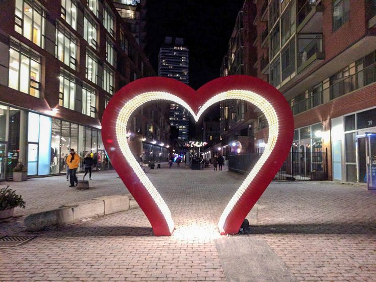 a large heart shaped sculpture in the middle of a city street at night with people walking around