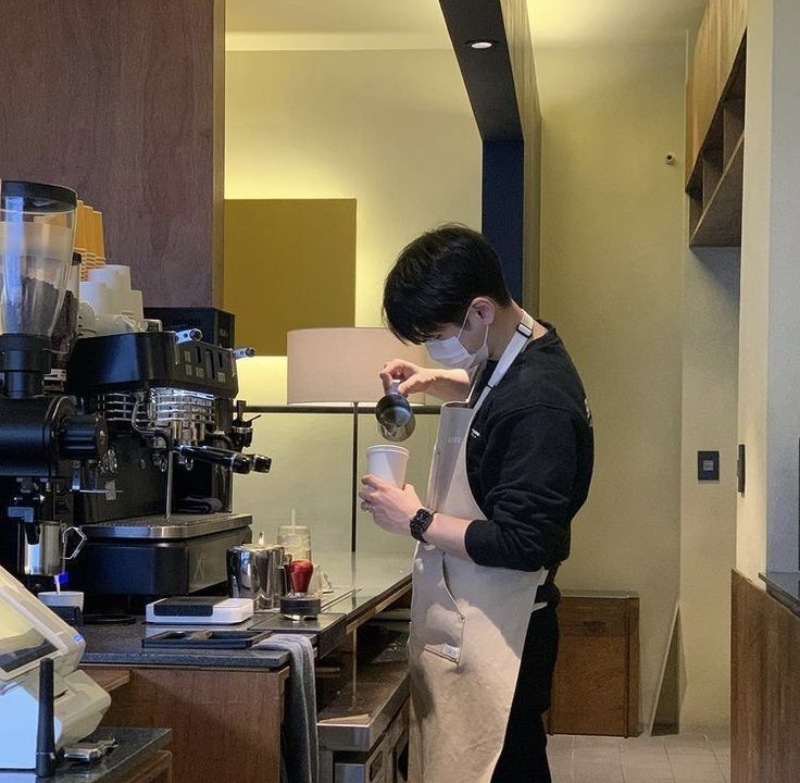 a man standing in front of a coffee machine while wearing a face mask and holding a cup