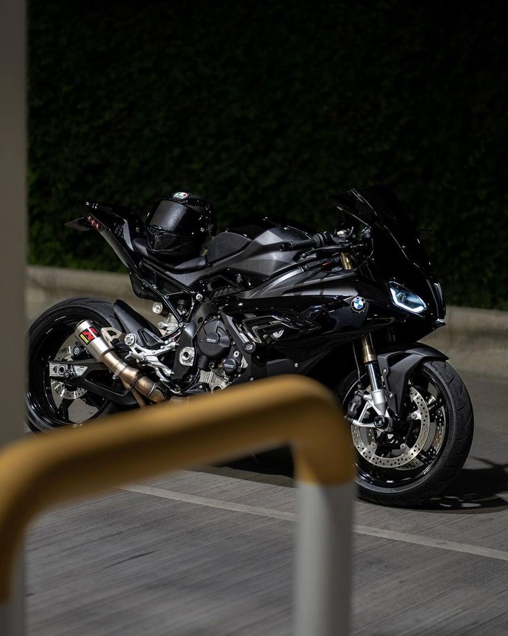 a black motorcycle parked on the side of a road next to a yellow rail and bushes