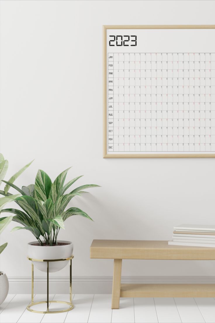 there is a calendar on the wall next to a bench and potted plant in front of it