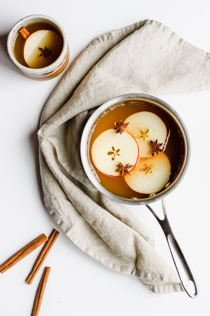 two bowls filled with apples and cinnamons on top of a white cloth next to spoons