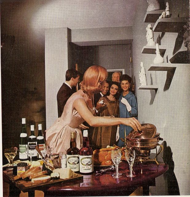 a group of people standing around a table with food and drinks on it in front of them