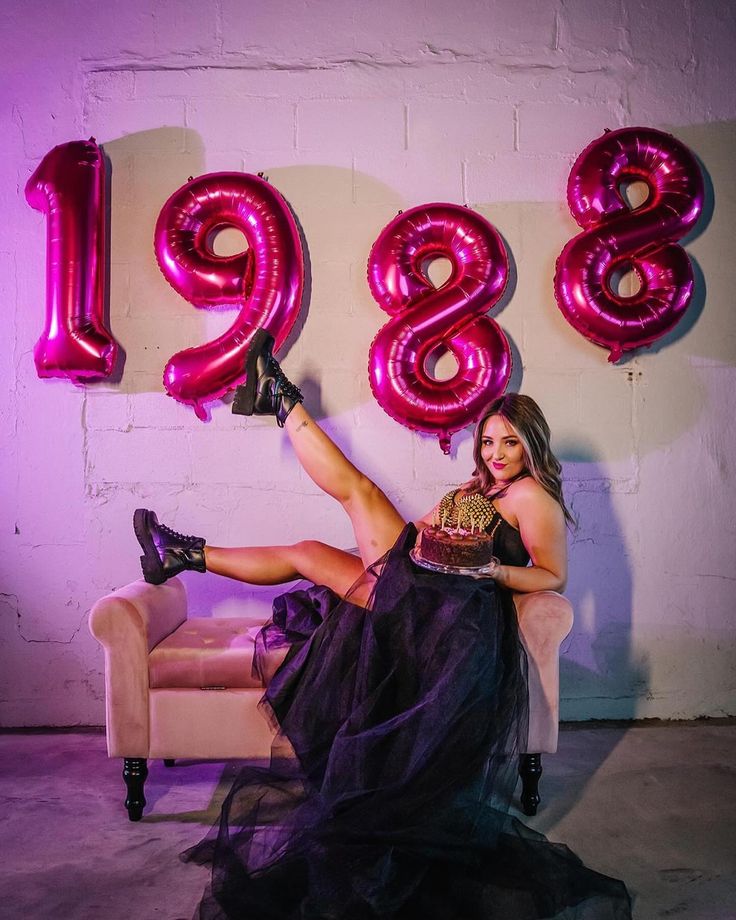 a woman is sitting on a couch in front of balloons that spell out the number eighteen