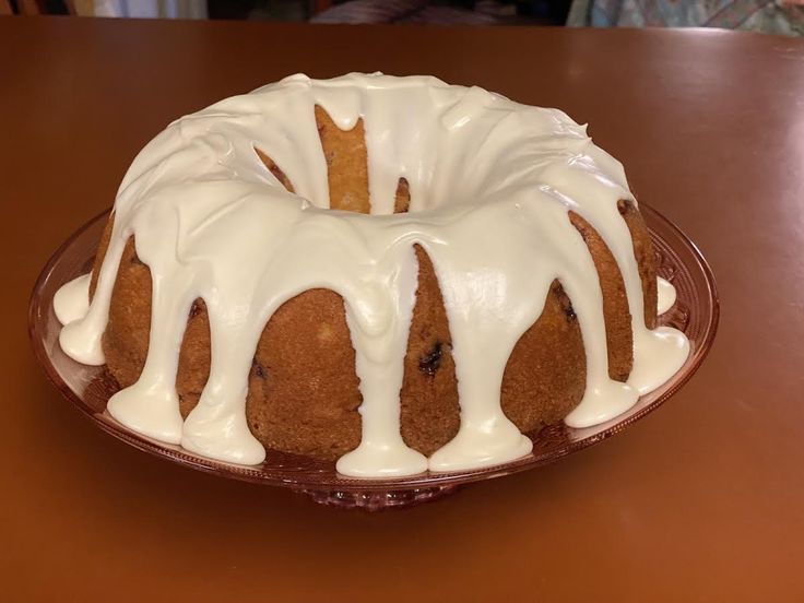 a bundt cake with white icing on a glass plate sitting on a table