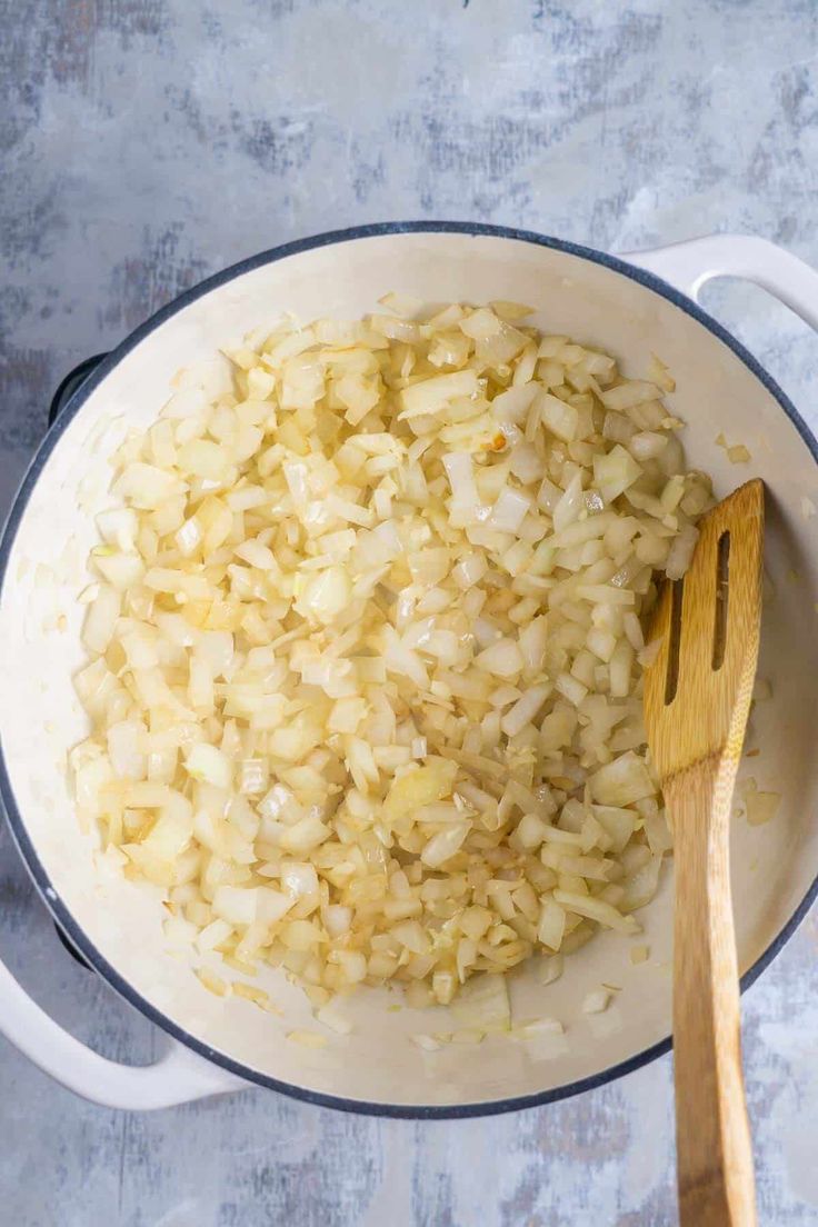 onions being cooked in a pot with a wooden spoon