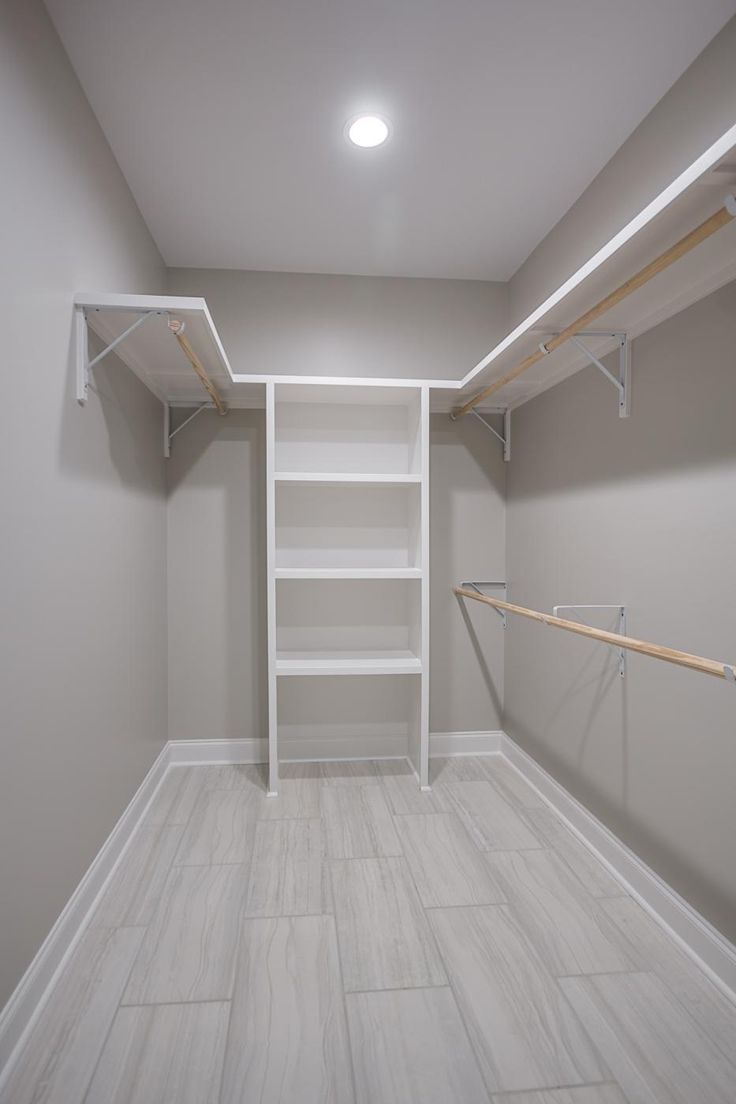 an empty walk in closet with white shelving and wooden rails on the wall,