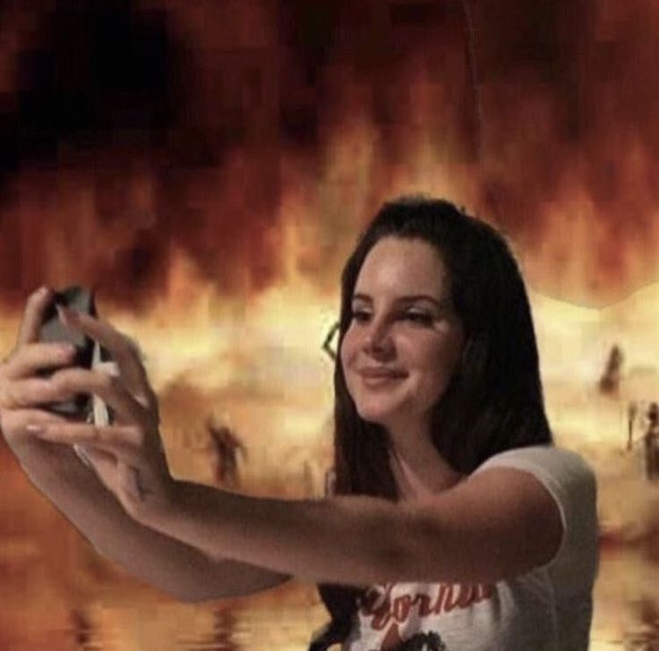 a woman taking a selfie with her cell phone in front of a large fire