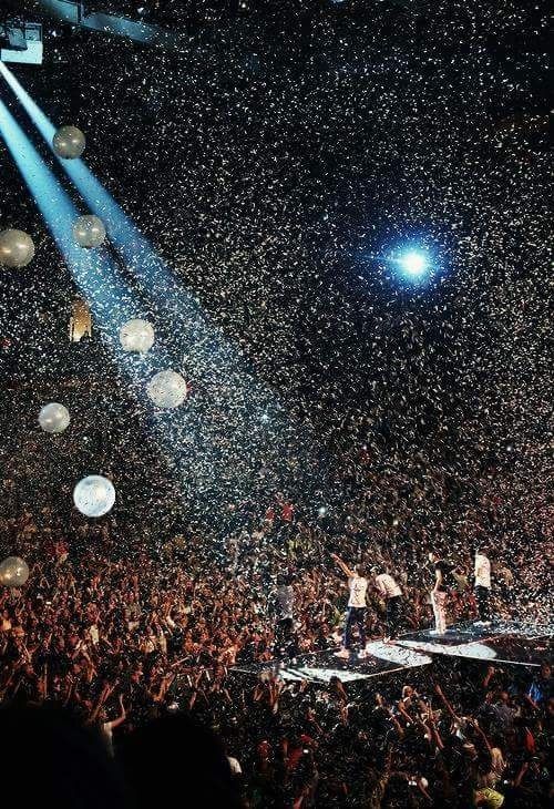 a large crowd at a concert with confetti falling from the ceiling and lights on