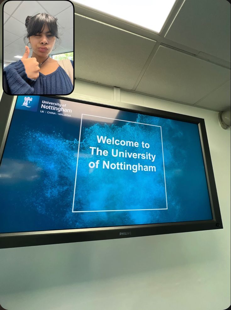 a woman giving a thumbs up in front of a large screen with the words welcome to the university of nottingham