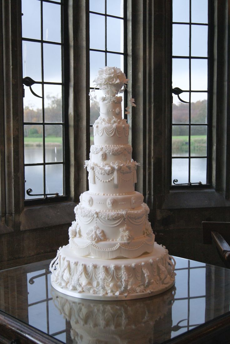 a large white wedding cake sitting on top of a table in front of two windows