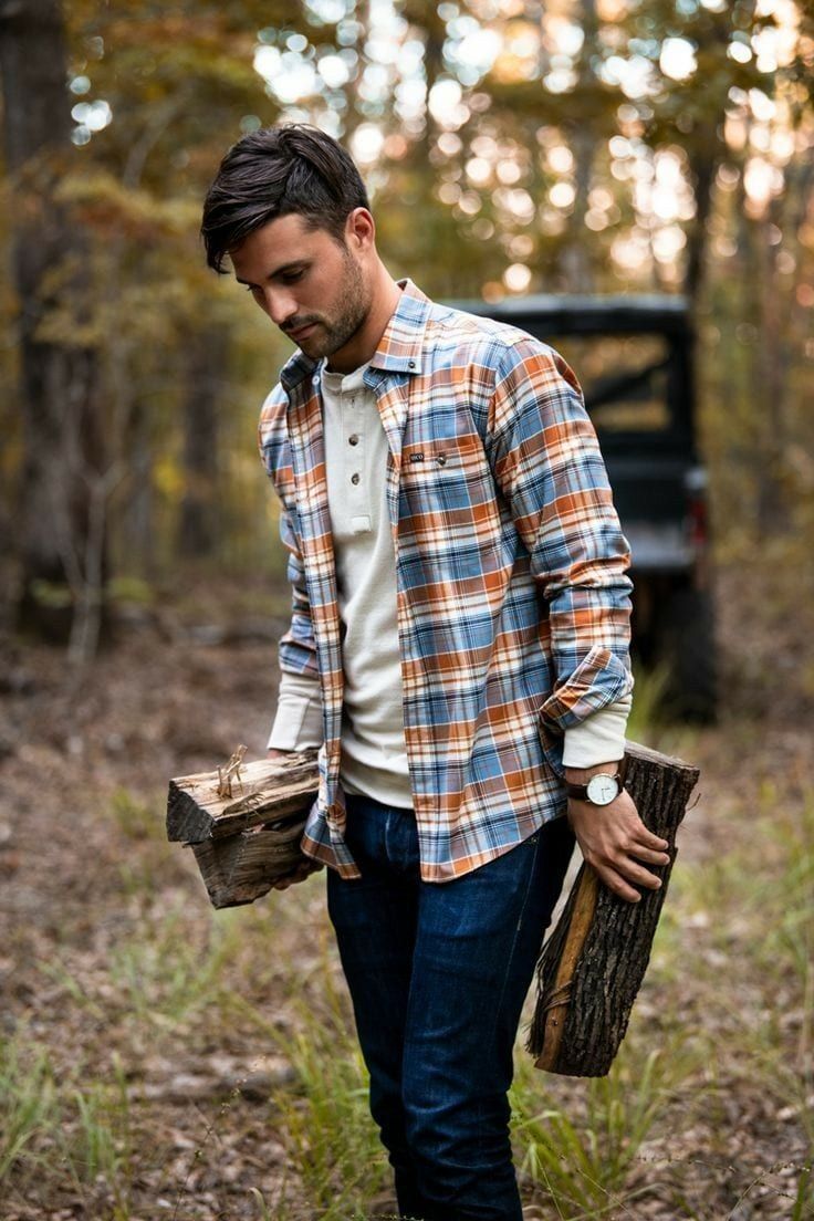 a man in plaid shirt and jeans walking through the woods holding a log with his hand