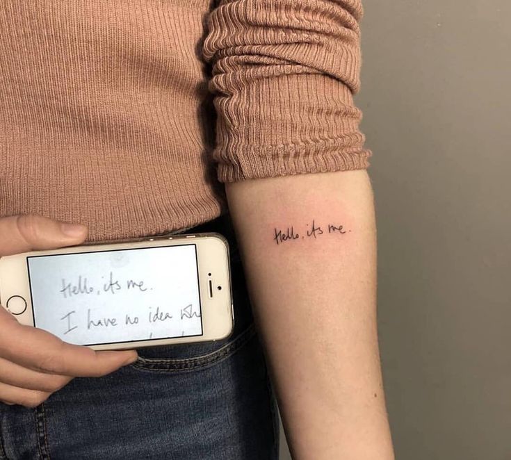 a woman with a small tattoo on her arm holding a cell phone in her hand