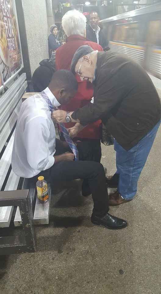 an older man sitting on a bench next to a younger man who is tying his tie